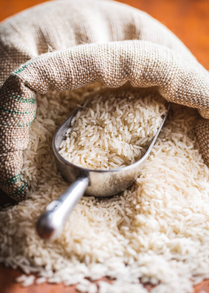 Uncooked white rice in a burlap sack on wooden table.